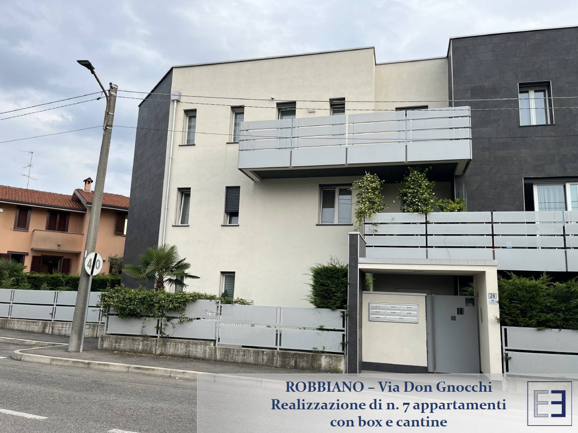 Esterno di un condominio con balconi e facciata bianca e grigia all'angolo di una strada.