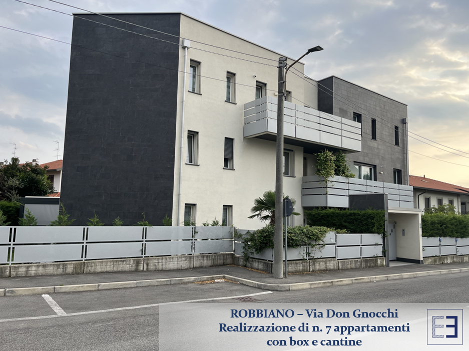 Moderno condominio con balconi, facciata bianca e grigia e lampione antistante.