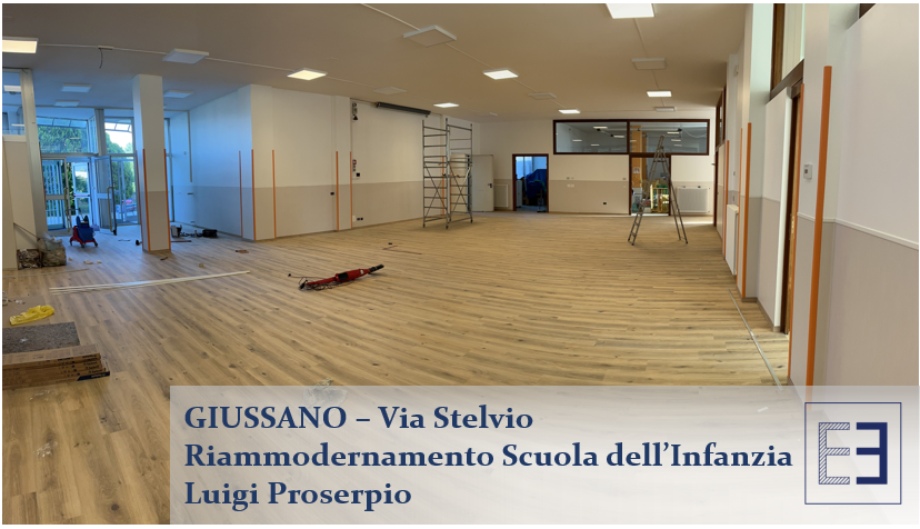 Ampio interno scolastico ristrutturato con pareti chiare, pavimento in legno e insegna con la scritta 