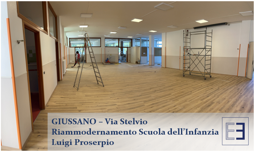 Sala scolastica vuota in fase di ristrutturazione con impalcature e pavimento in legno, con la scritta Giussano Via Selvio in italiano.