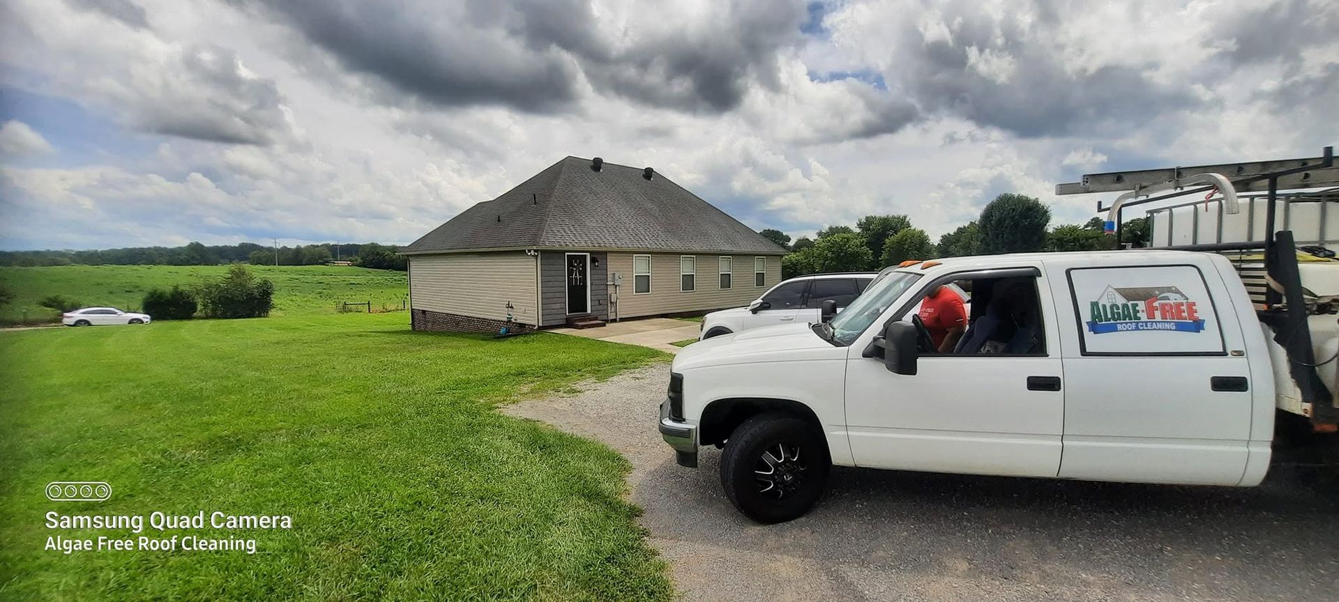 White pickup truck parked beside a beige house on a green lawn under cloudy skies.
