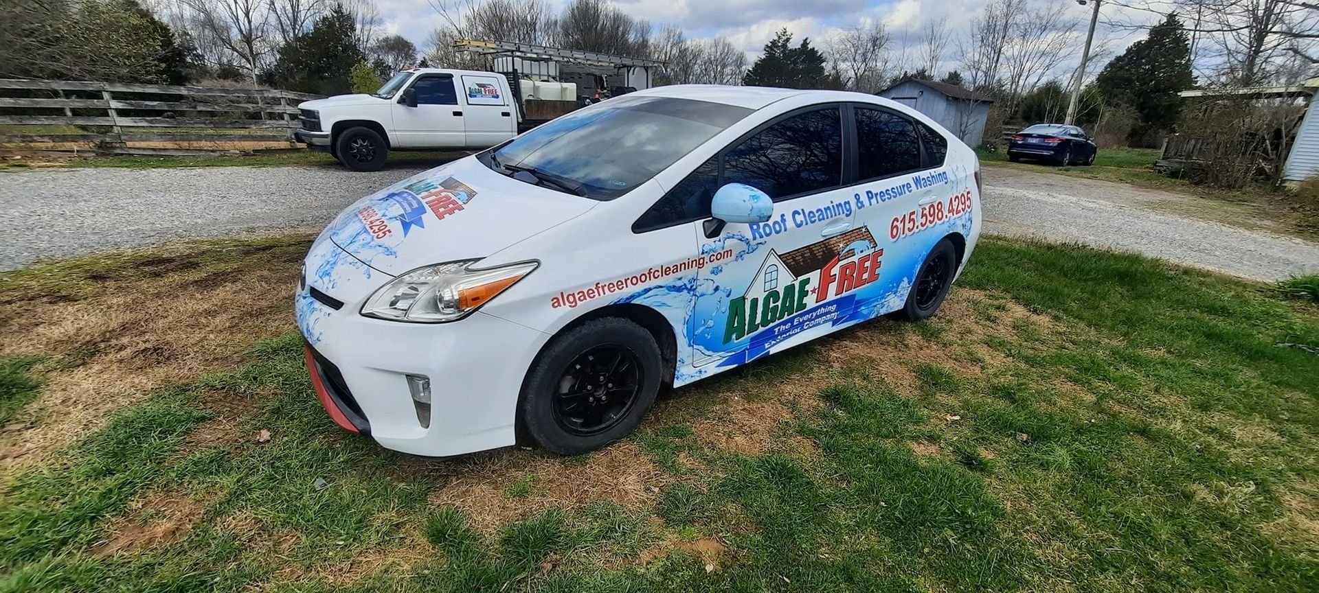 White race car with colorful decals parked on grass near a road, with a white pickup truck behind it