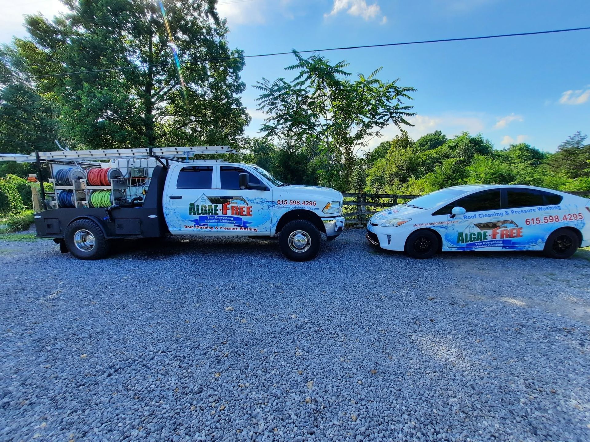 Service truck and white sedan parked on gravel road, both with company logos in a sunny outdoor area