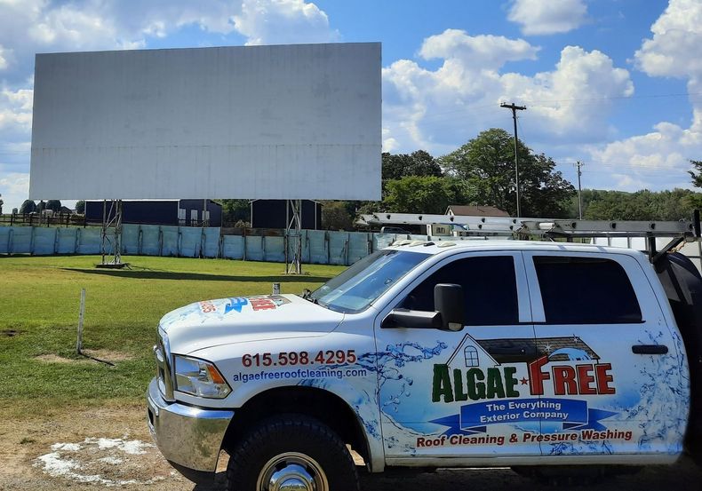 White service truck with “ALGAE FREE” logo parked by a large blank billboard in a grassy field.