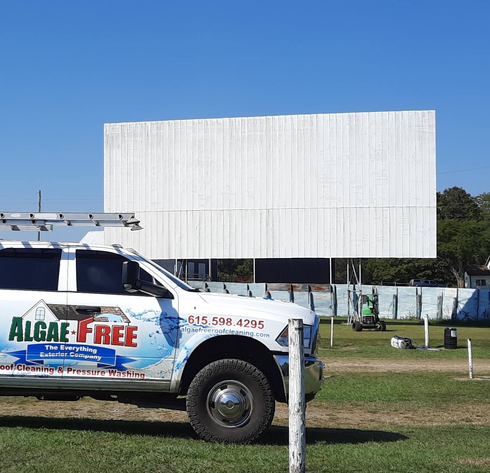 White outdoor screen at a drive-in with a white Algae-Free service truck in front on a grassy lot.