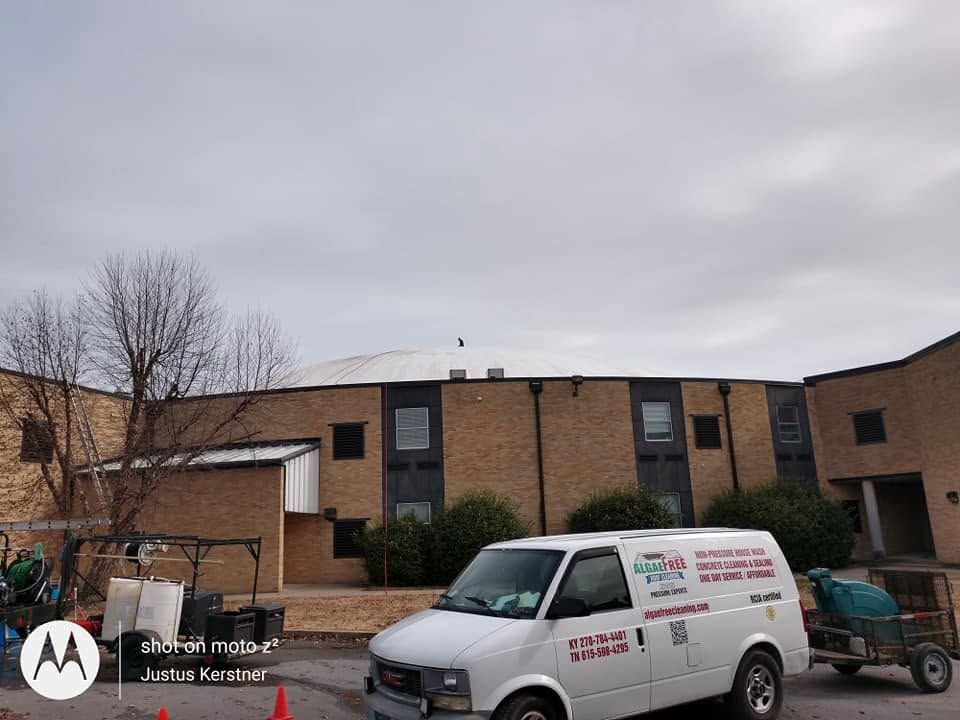 Brick building exterior with a white work van and trailer parked under a cloudy sky