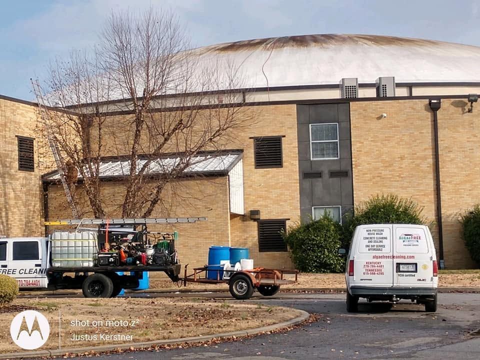 Apartment building exterior with parked utility truck and white van, leafless tree in front