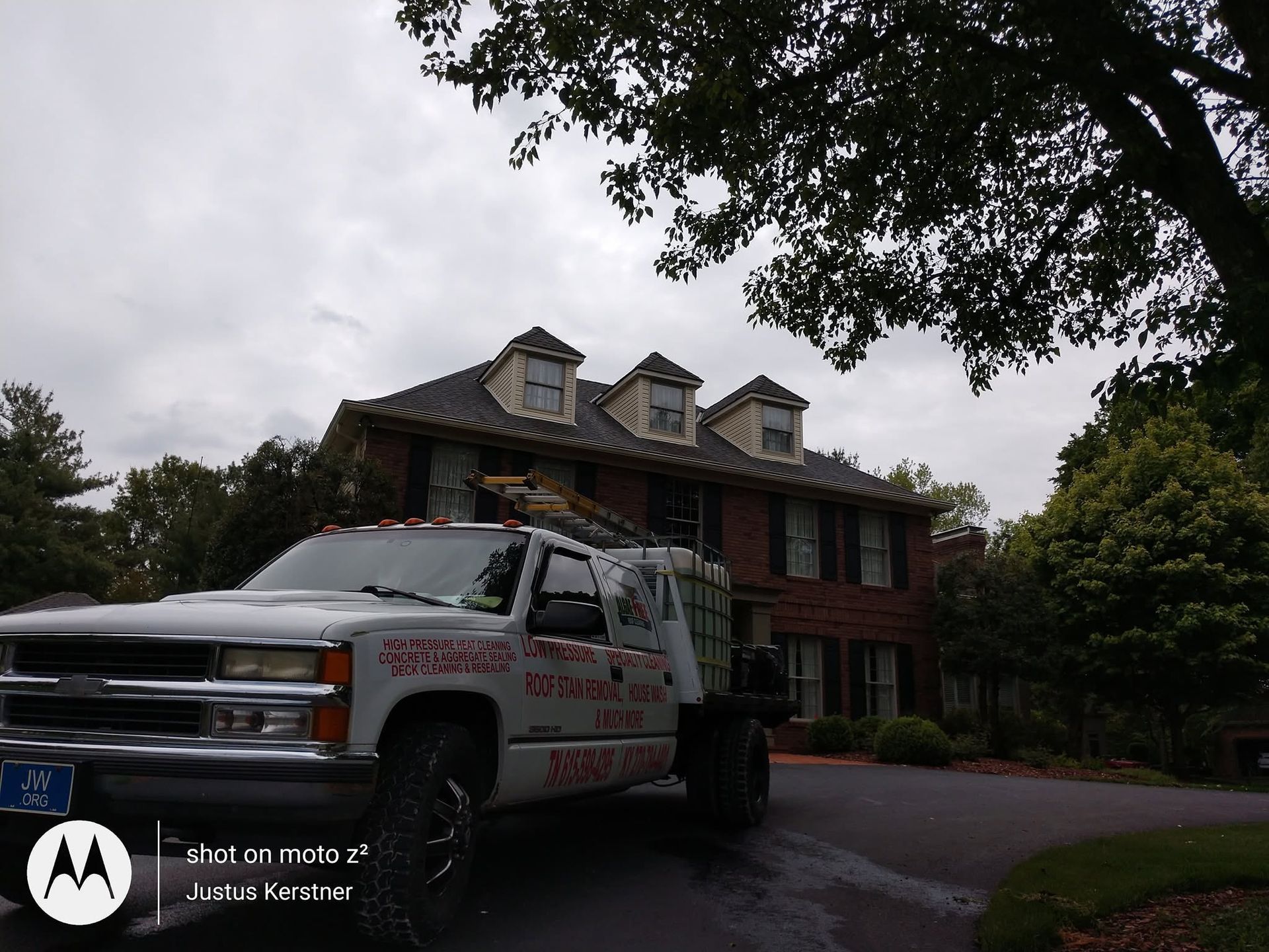 White utility truck parked in front of a brick house with dormer windows under a cloudy sky