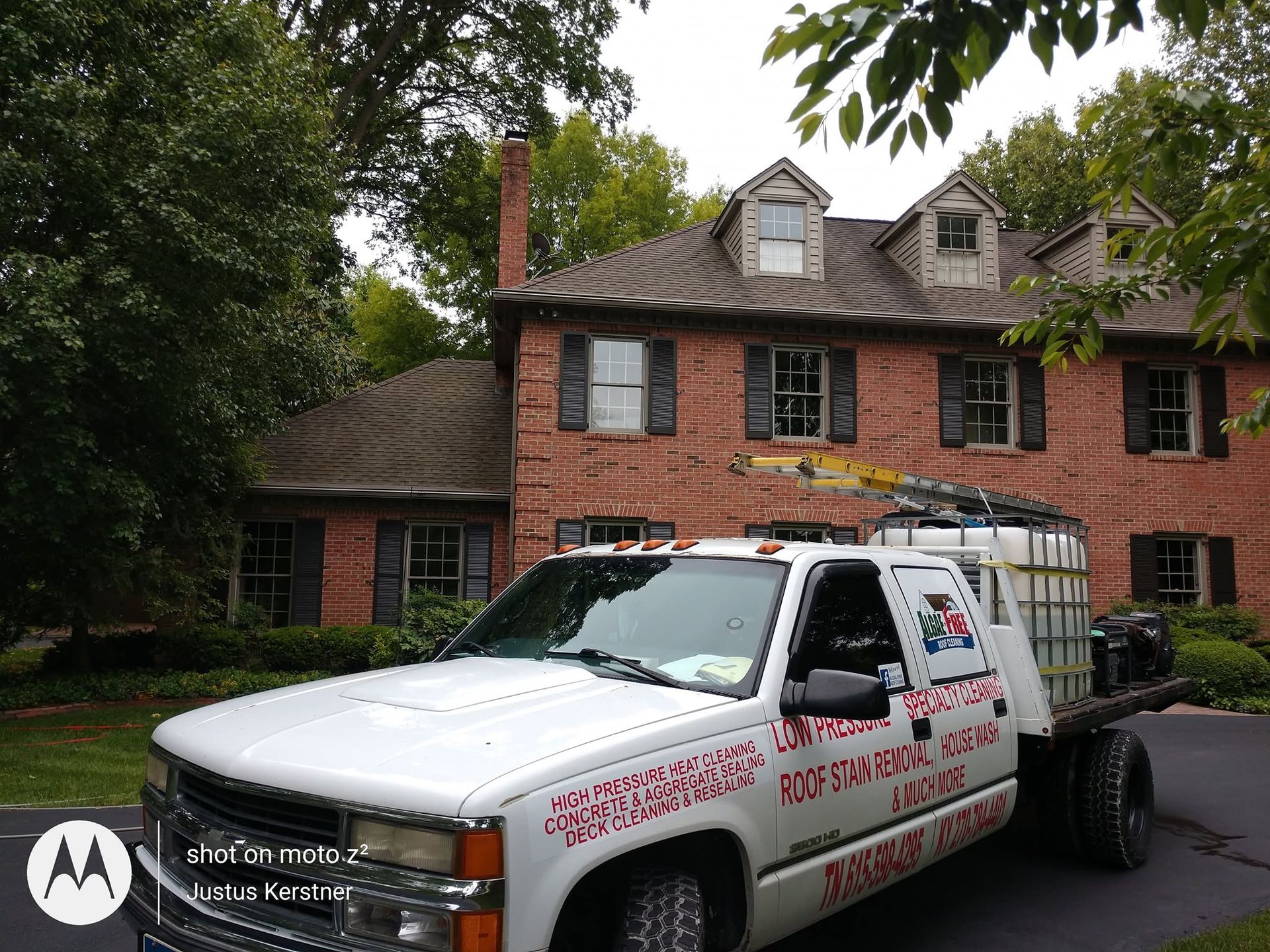 White tow truck parked in front of a brick house with trees overhead