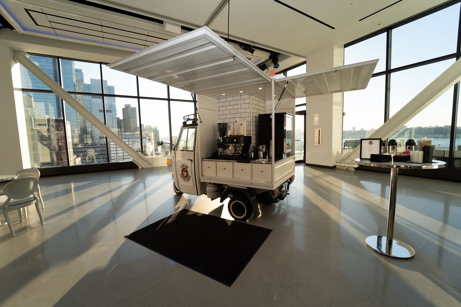 A white truck is parked in a large room with lots of windows.