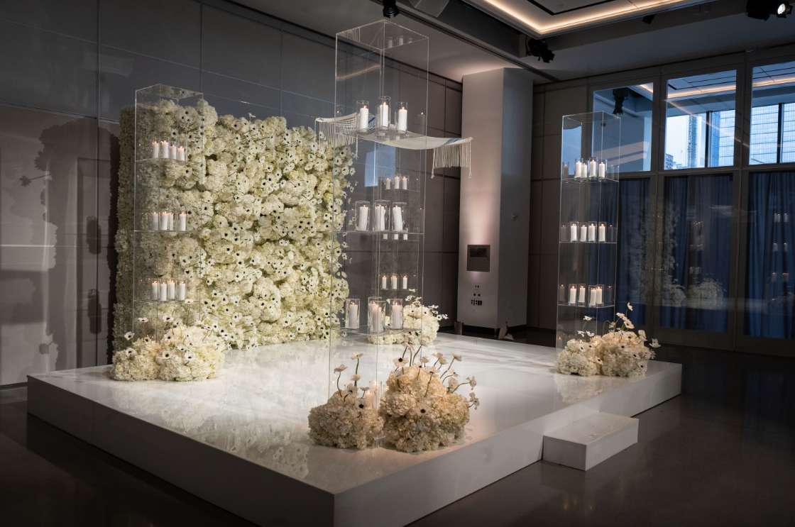 a room with a stage and a wall of white flowers .