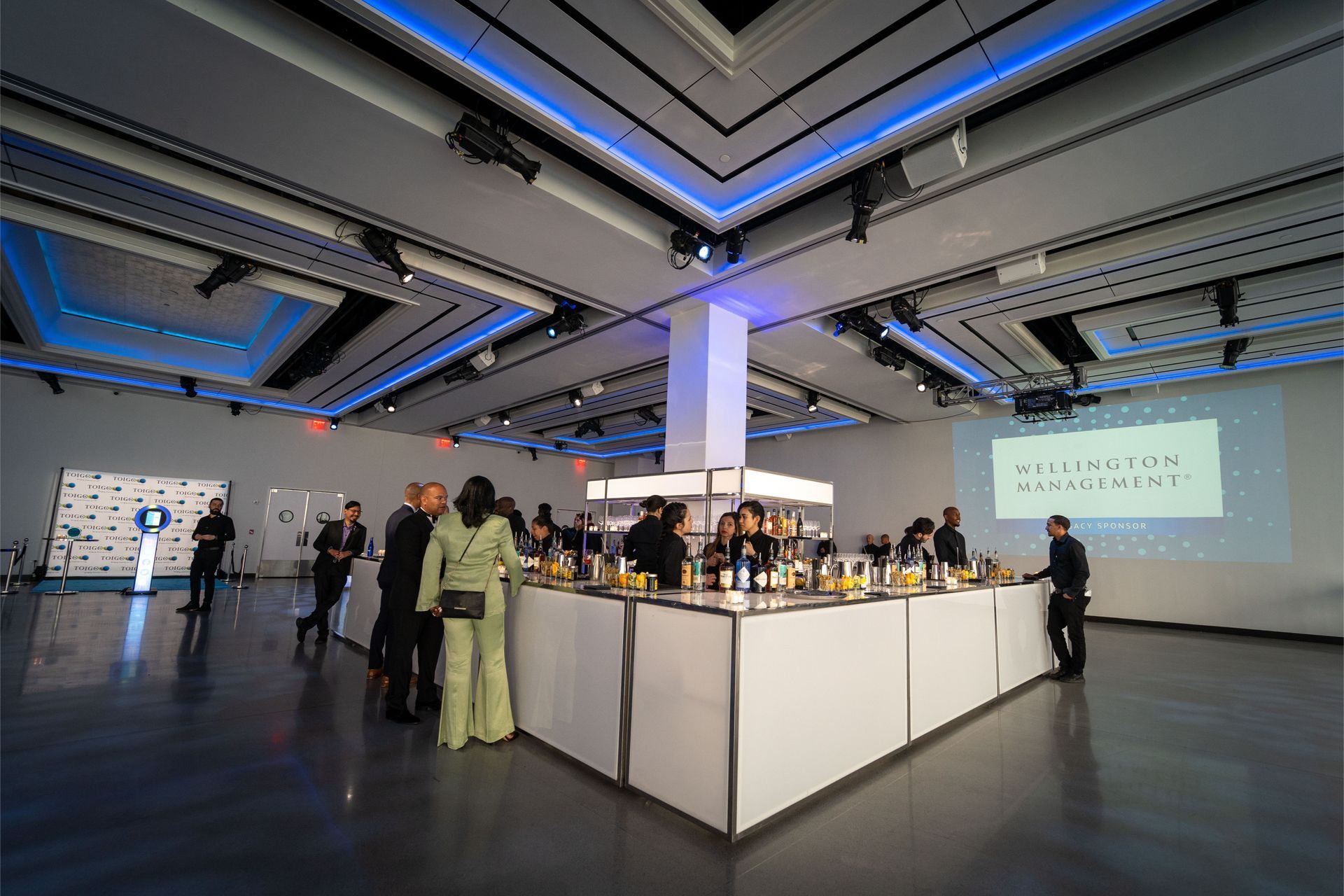 A group of people are standing around a bar in a large room.