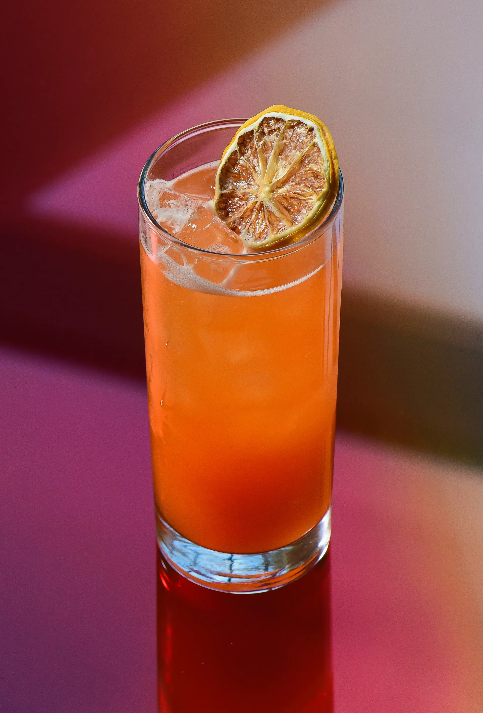 A tall glass of orange liquid with a straw and a lemon slice on top