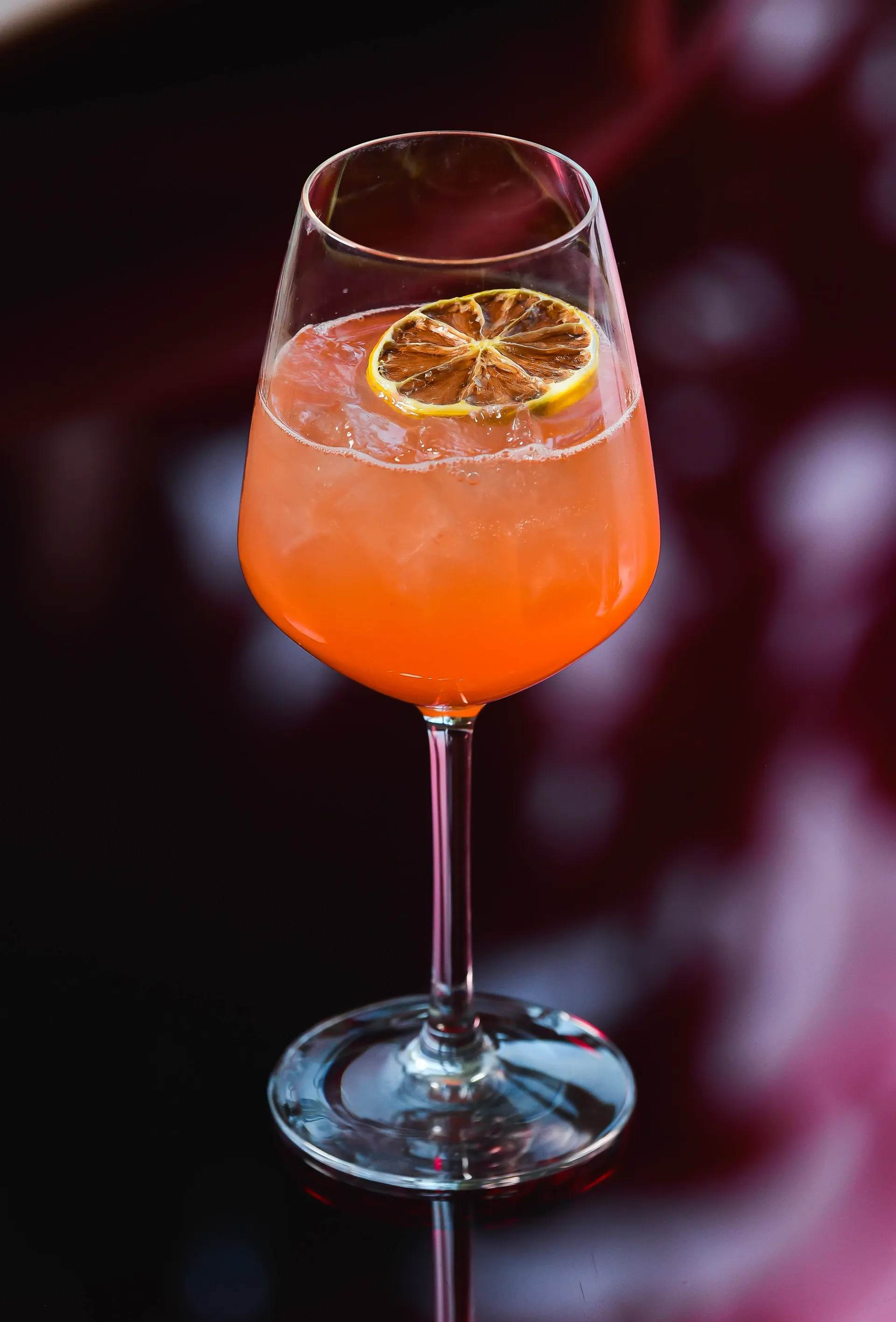 A tall glass of orange liquid with a straw and a lemon slice on top