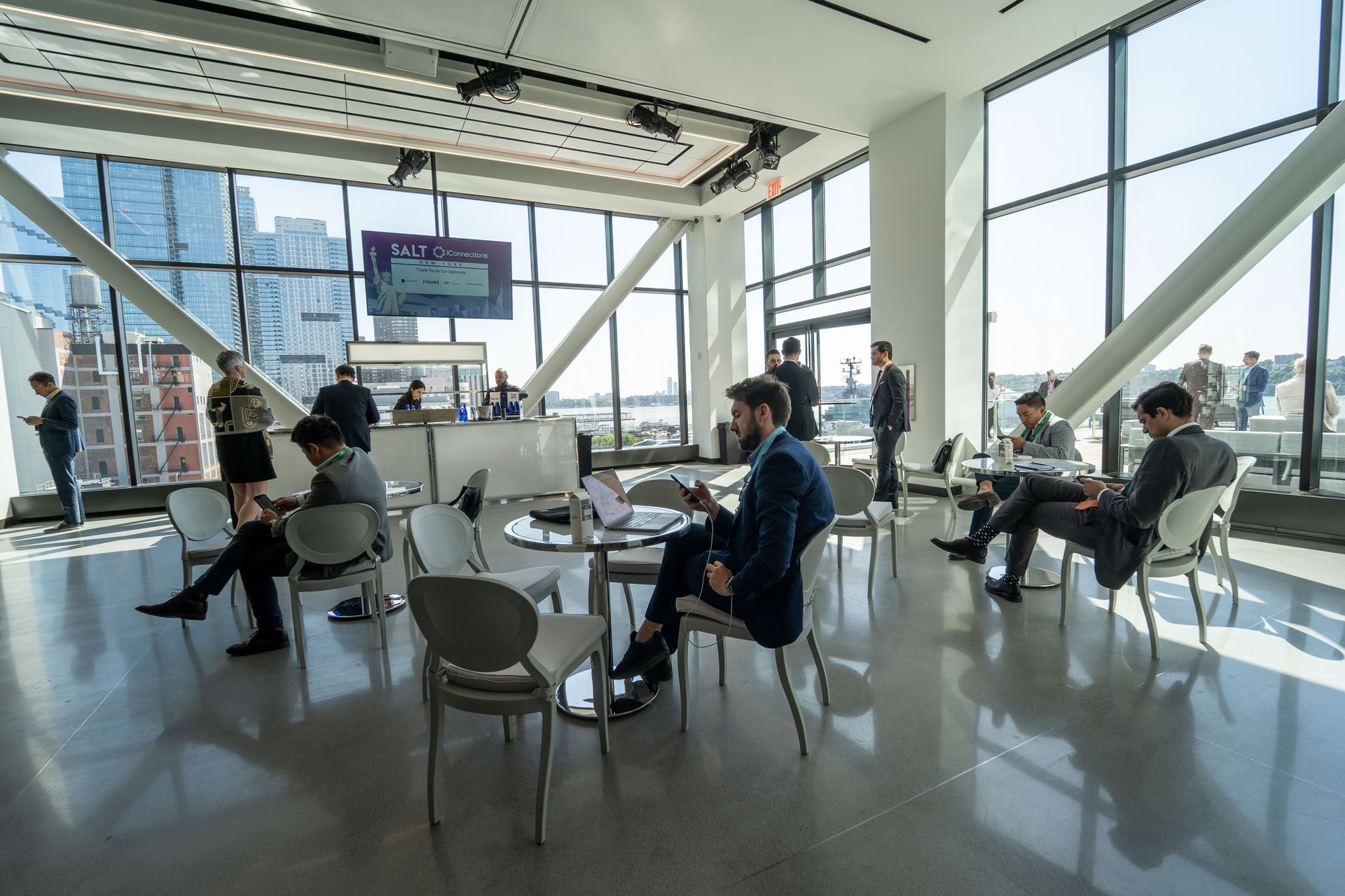 A group of people are sitting at tables in a room with a lot of windows.