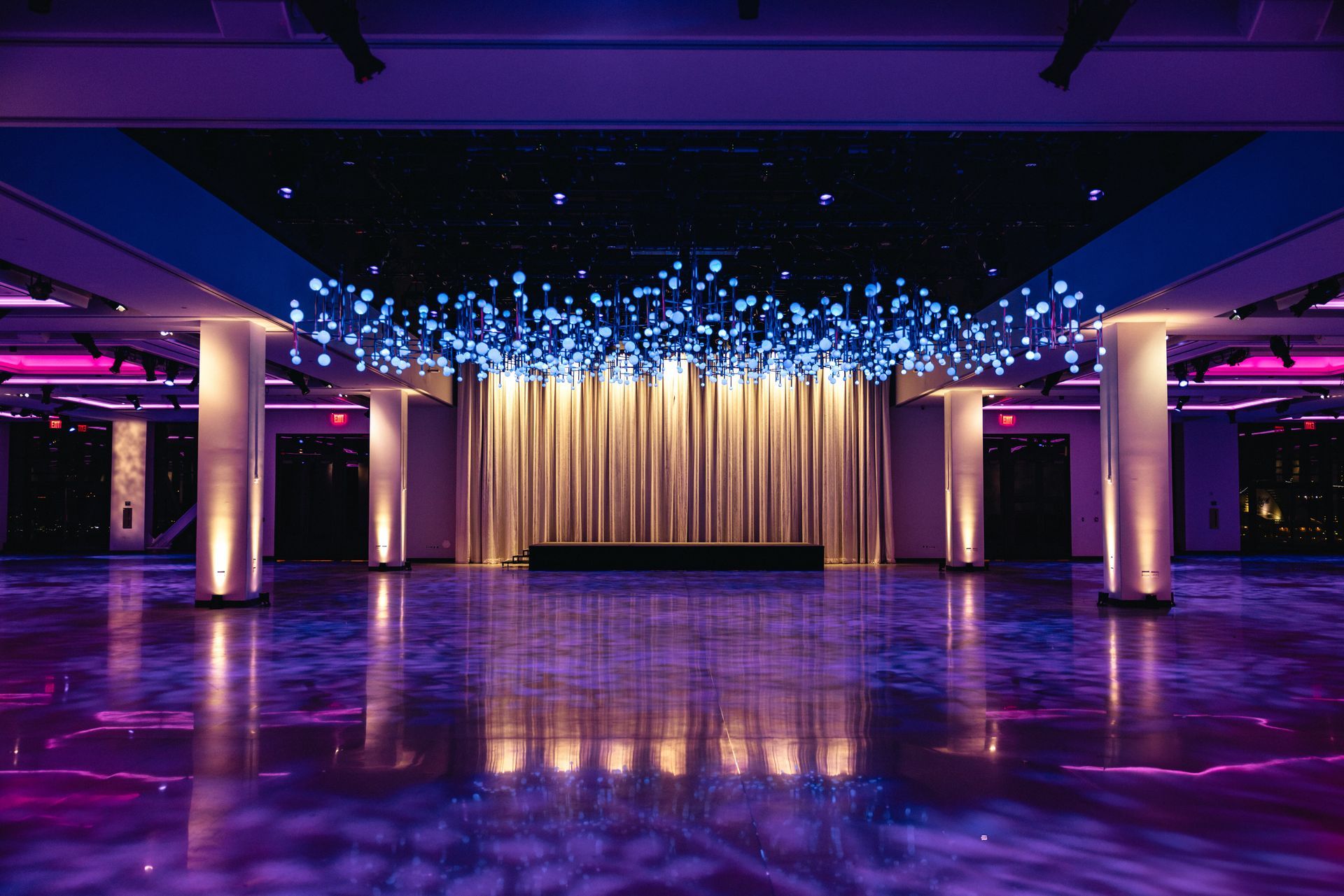 Large event space with purple and blue lighting, gold curtains, and reflective floor.