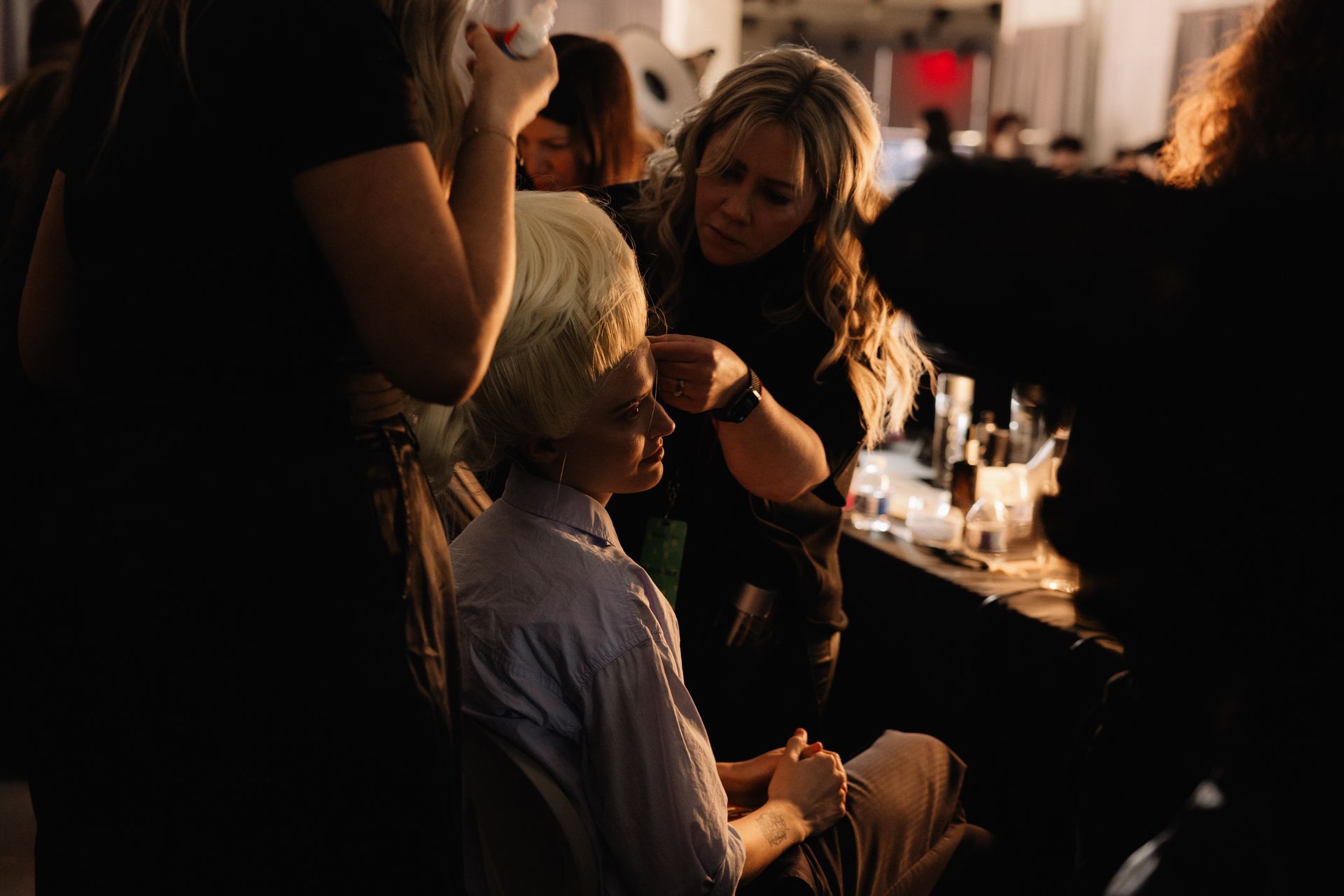 Makeup artist applies makeup to a person’s face, backstage at an event.