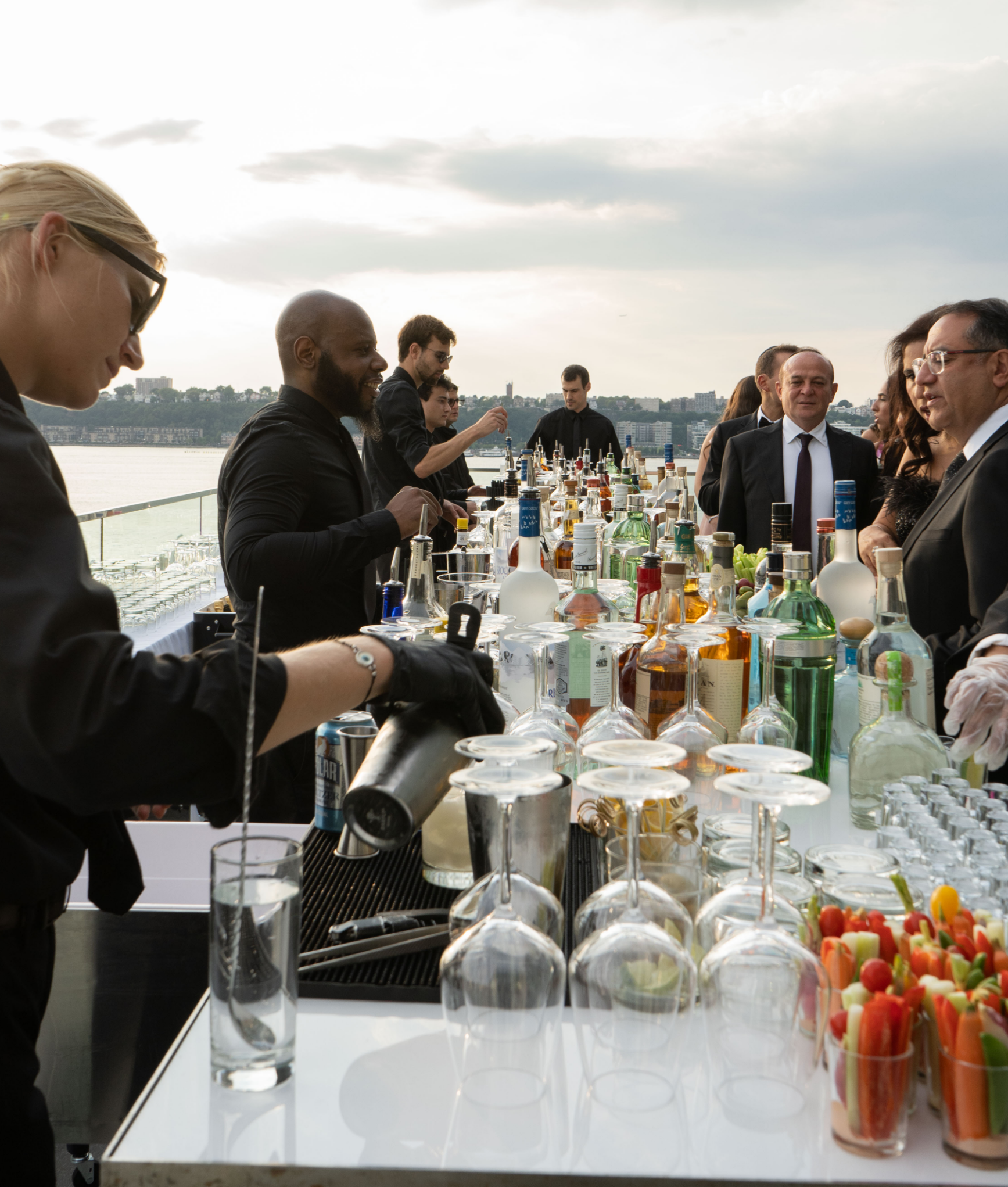 A group of people are gathered around a table filled with bottles and glasses.