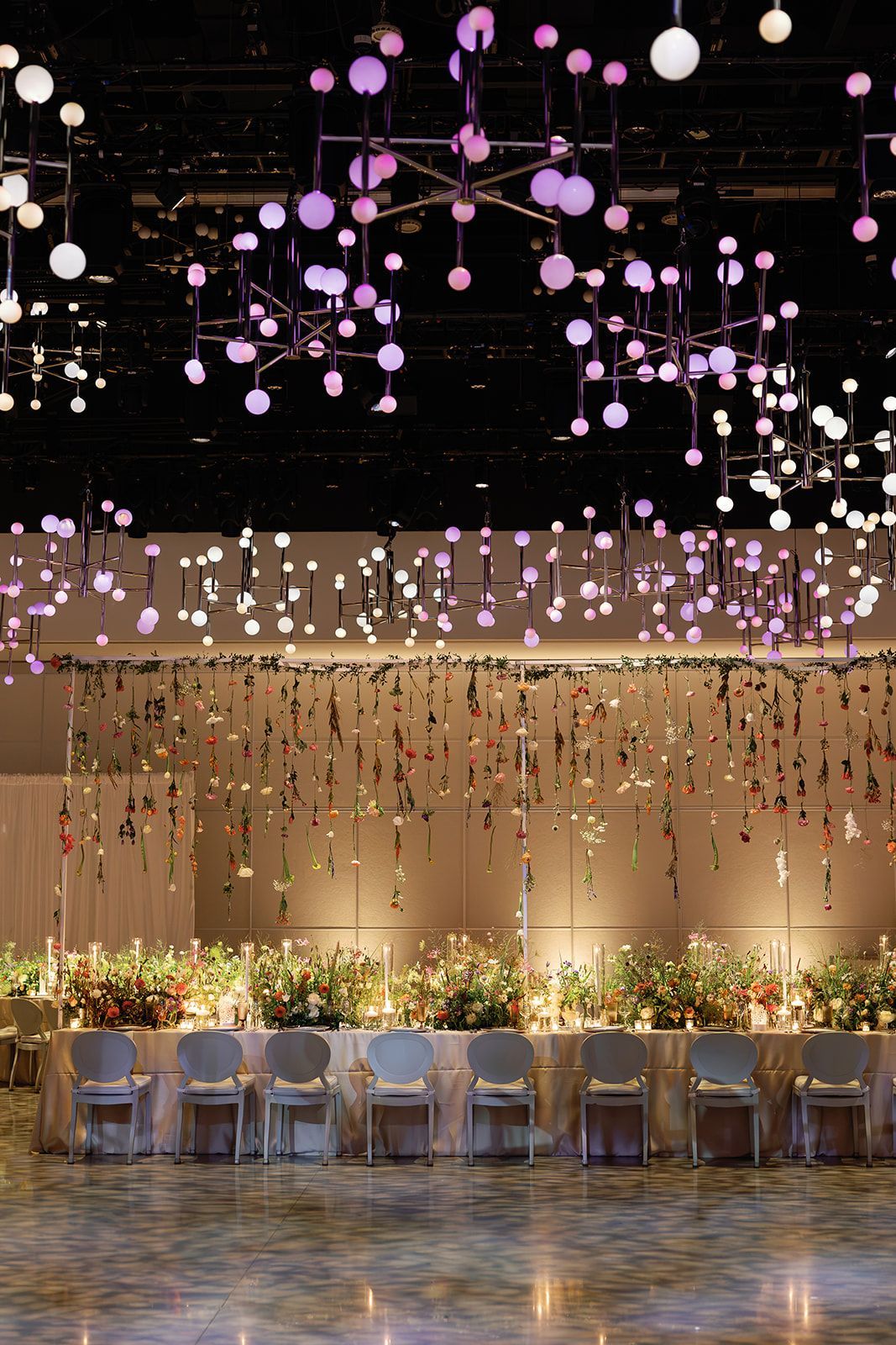 Elegant event hall with hanging purple lights, warm gold backdrop, and rows of chairs along a polished floor