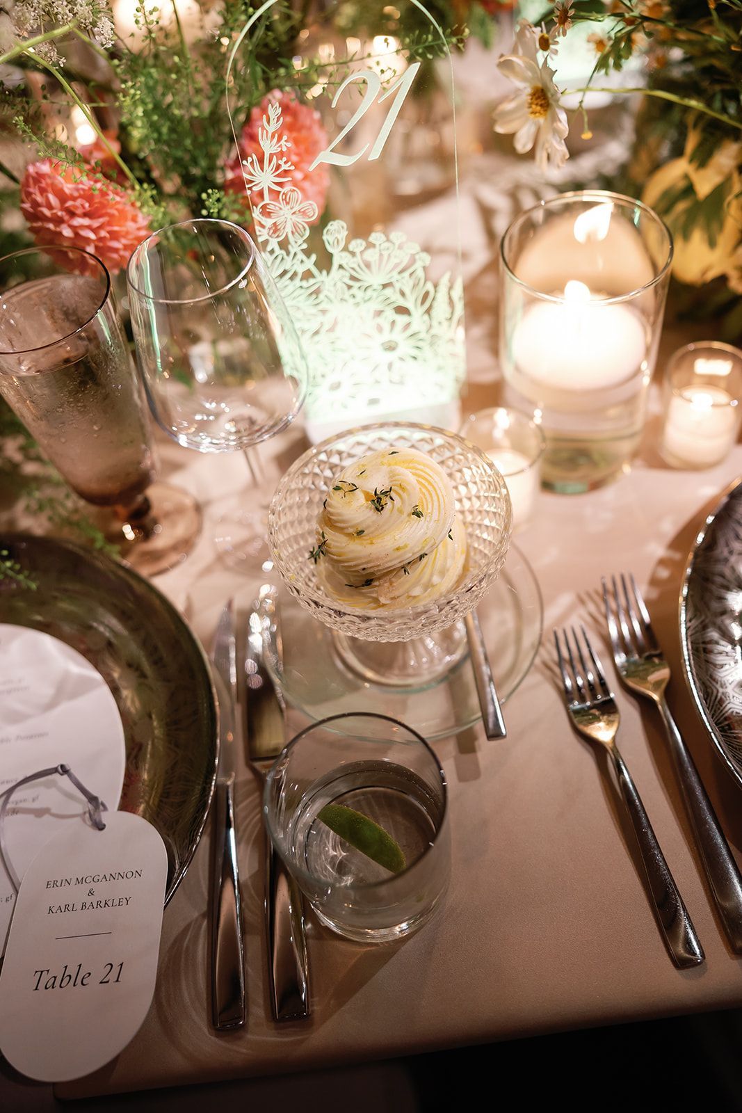 Elegant candlelit table setting with clear glassware, pink flowers, silverware, and a decorated dessert centerpiece