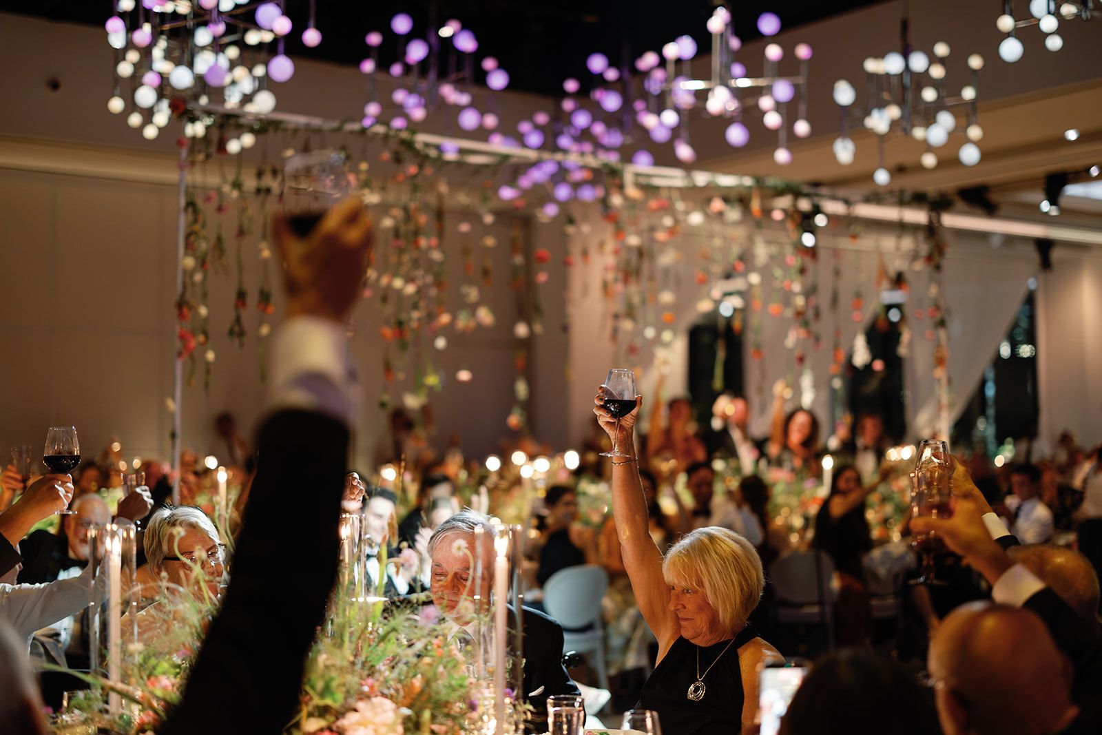 Elegant banquet hall with guests dining under hanging lights and purple floral decor