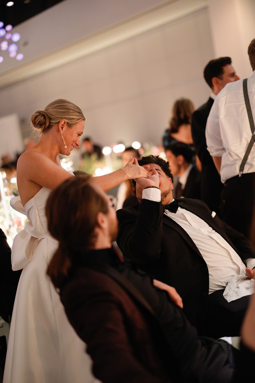 Wedding reception with guests seated as a bride leans in to speak to a man in a black suit.