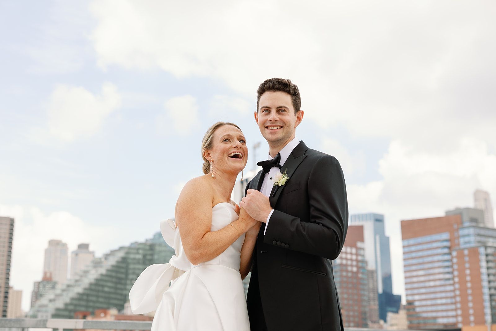 Smiling bride and groom pose together on a city rooftop with skyline buildings in the background