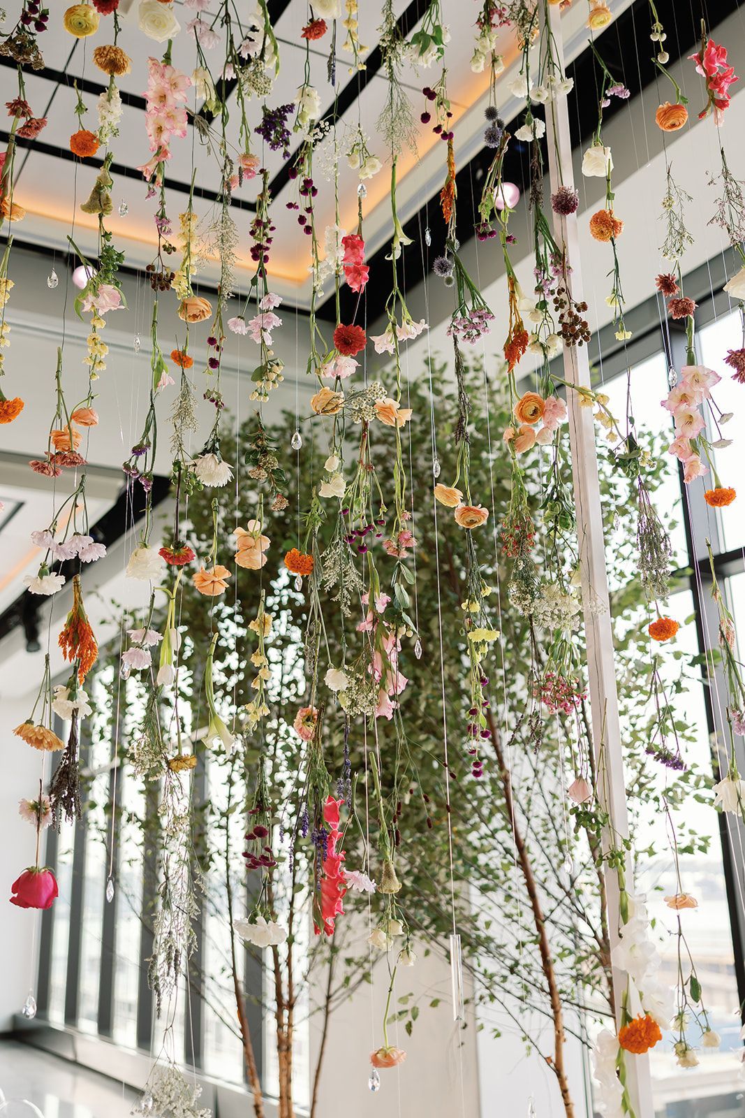 Hanging floral installation with cascading green vines and red, orange, and white flowers indoors