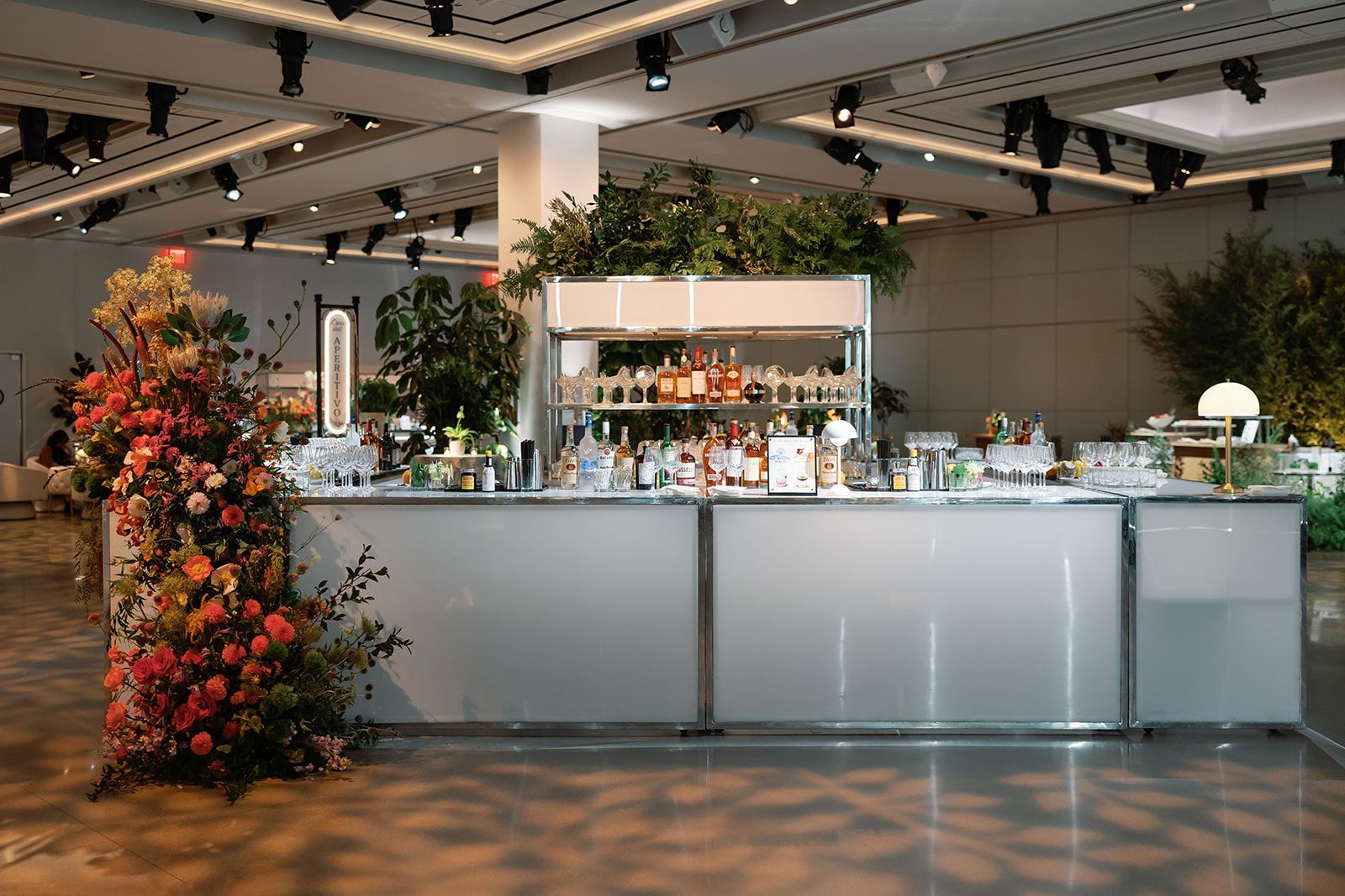 Modern bar counter with bottles, plants, and autumn floral arrangement in a bright indoor venue