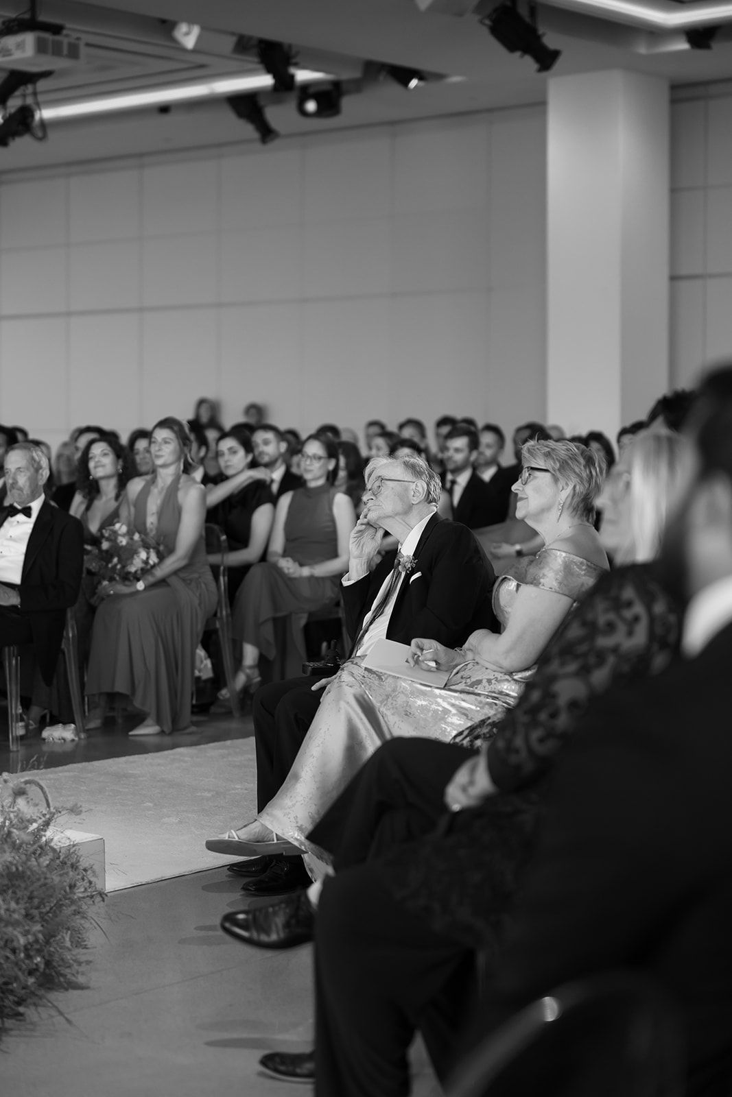 Crowd seated and standing at a formal indoor event, watching a stage off to the left.