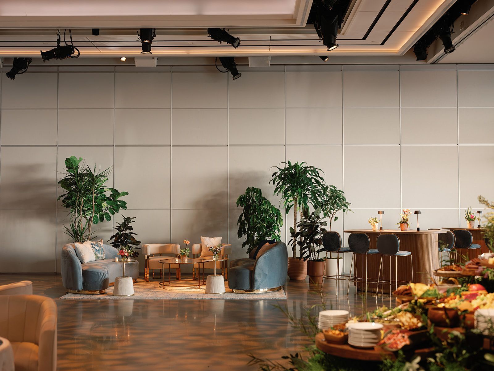 Modern lounge with blue chairs, potted trees, warm lighting, and a long dining table in a spacious room