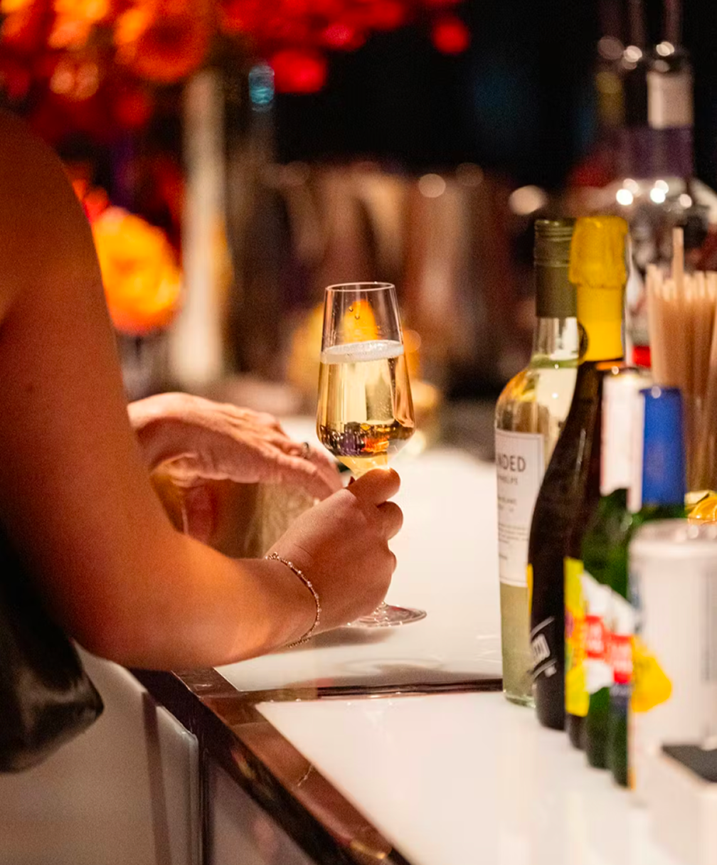 Hand pouring champagne at a bar with bottles and glasses on the counter