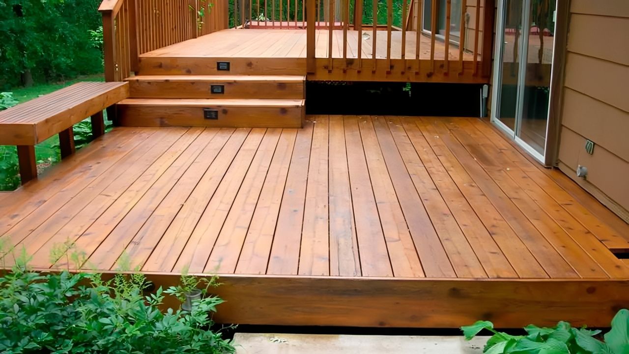 Wooden backyard deck with steps, railings, and green shrubs at the edge.