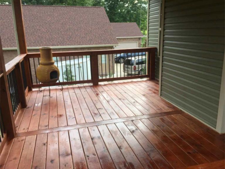 A newly stained wooden deck with black metal railings, a clay chiminea, and green siding on the adjacent house wall.