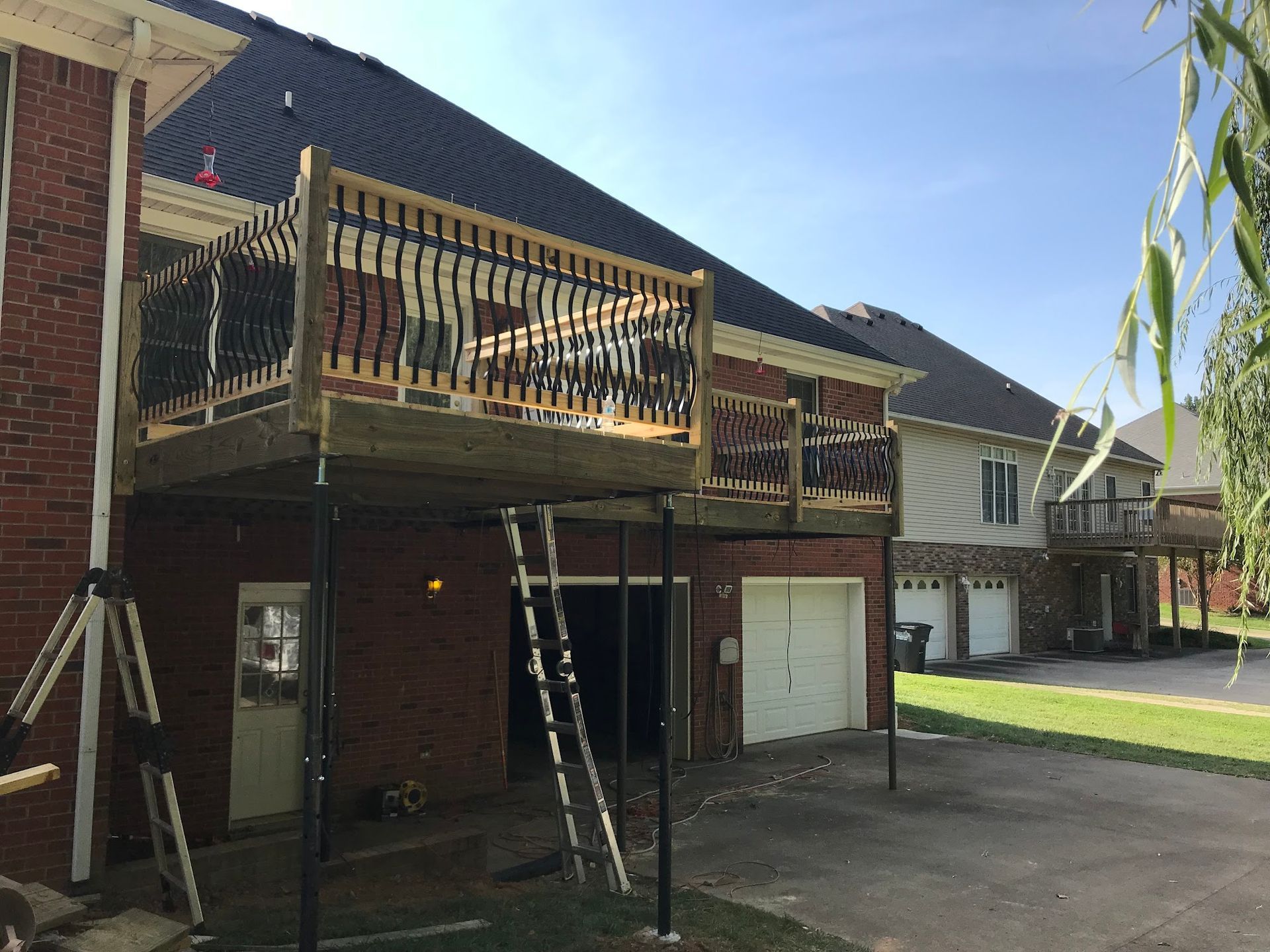 A raised wooden deck is under construction on the back of a brick house, supported by black metal poles.