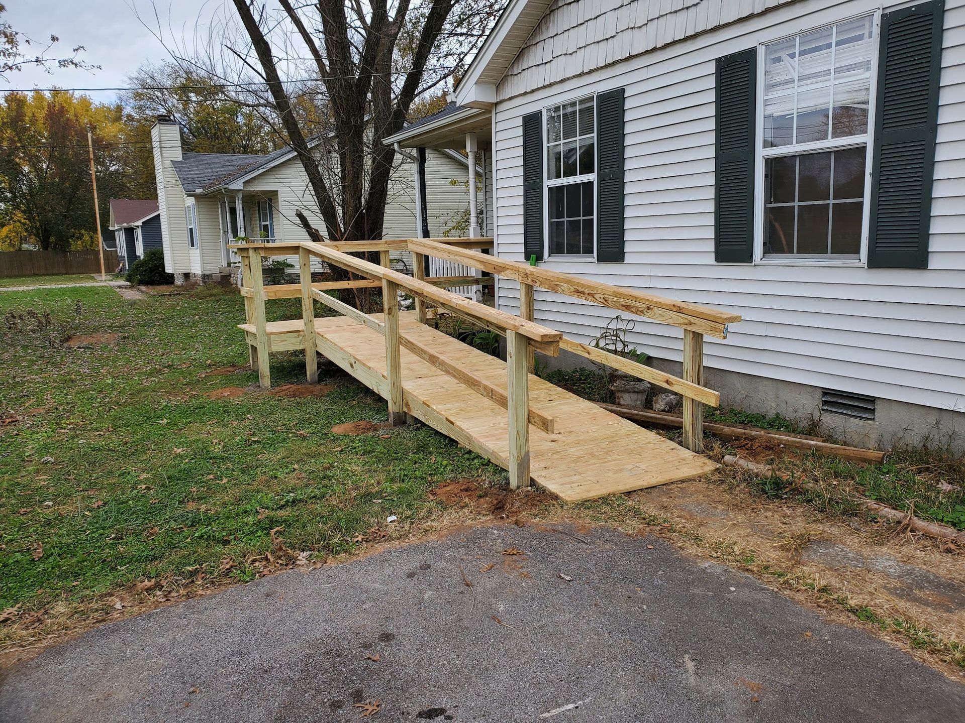 A wooden wheelchair ramp leading to the front entrance of a white house with dark green shutters.