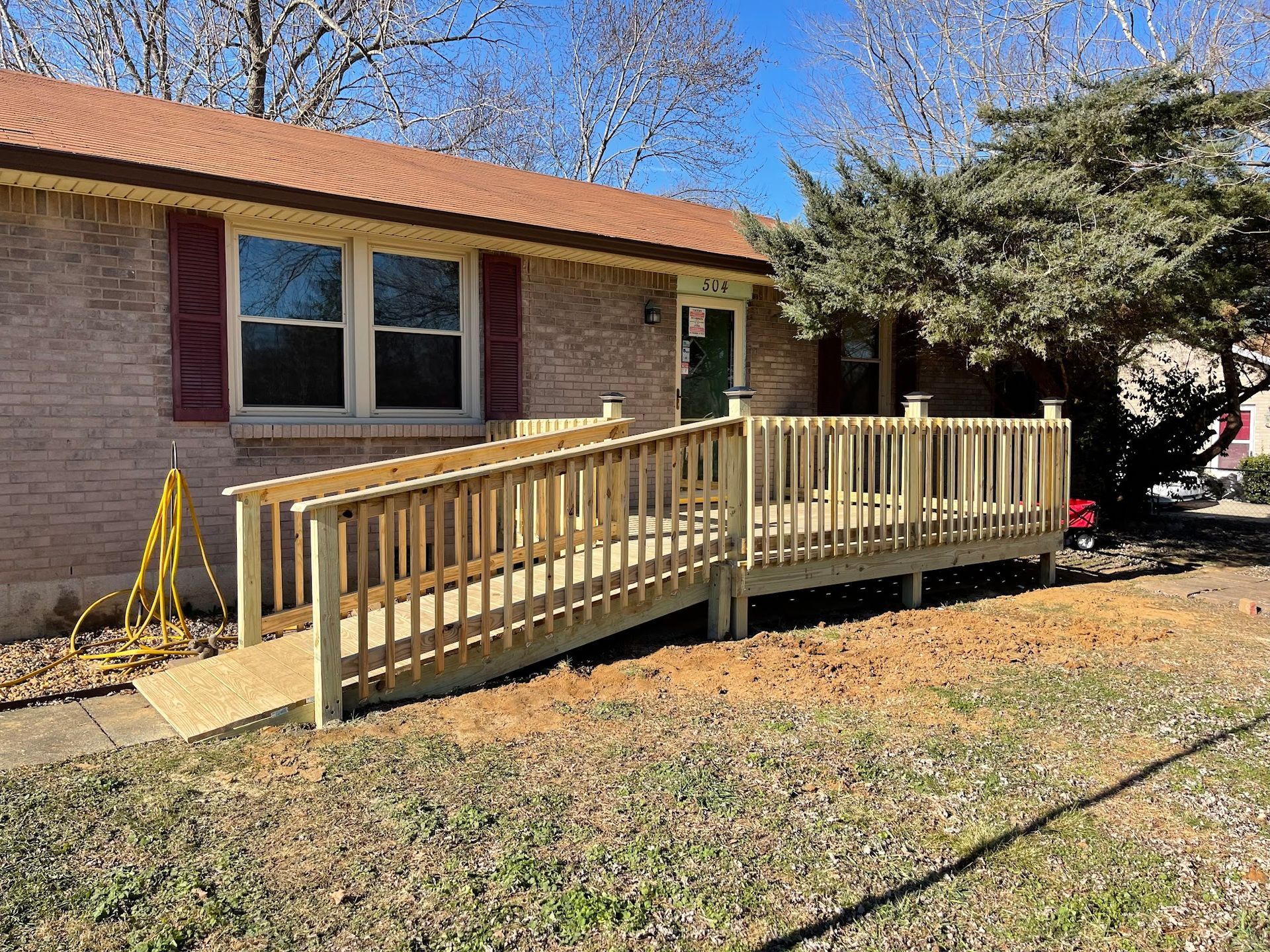 A wooden wheelchair ramp with railings installed in front of a brick house.