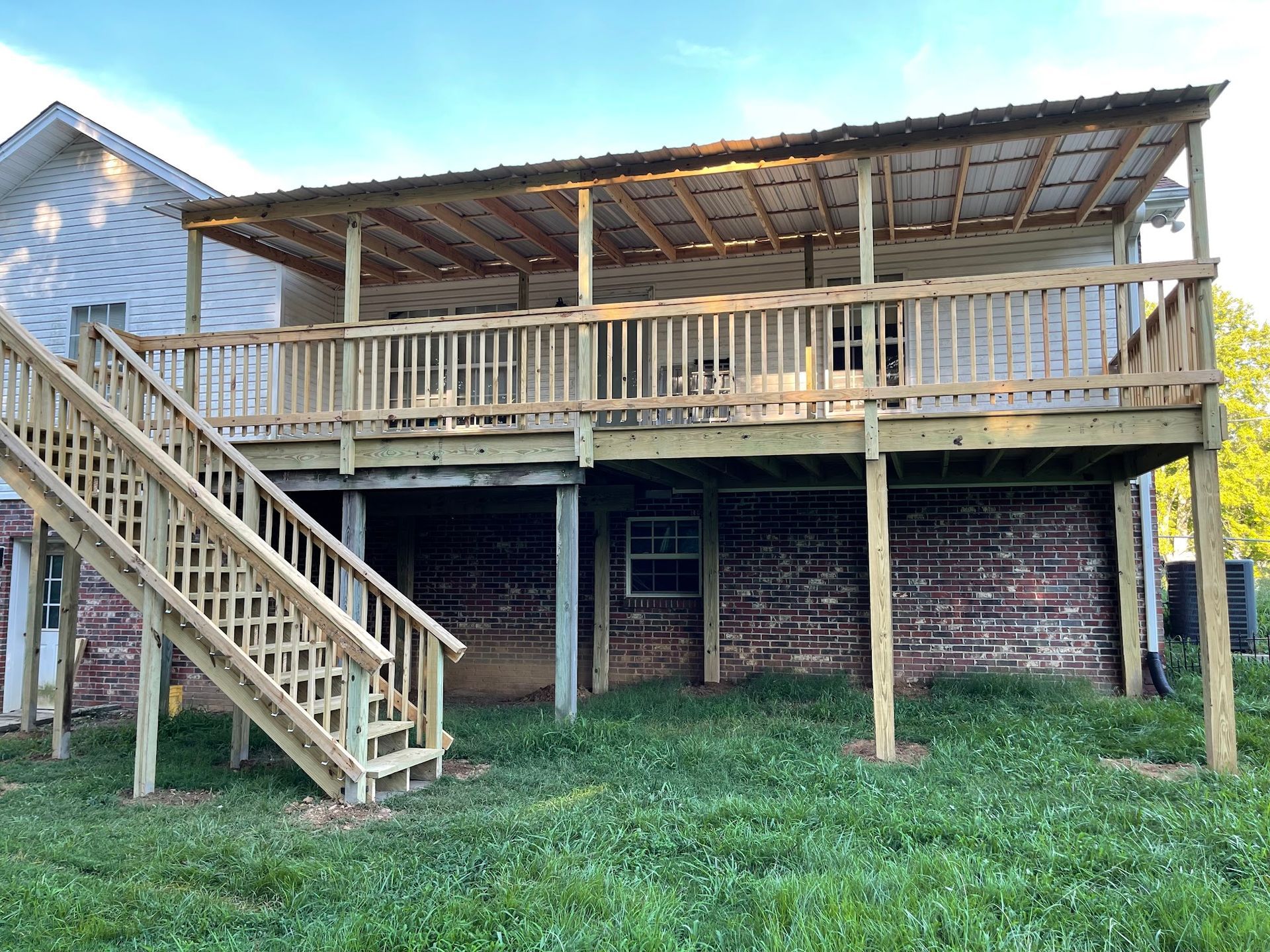 A newly constructed wooden deck with a covered roof and stairs attached to the back of a house with a stone foundation.