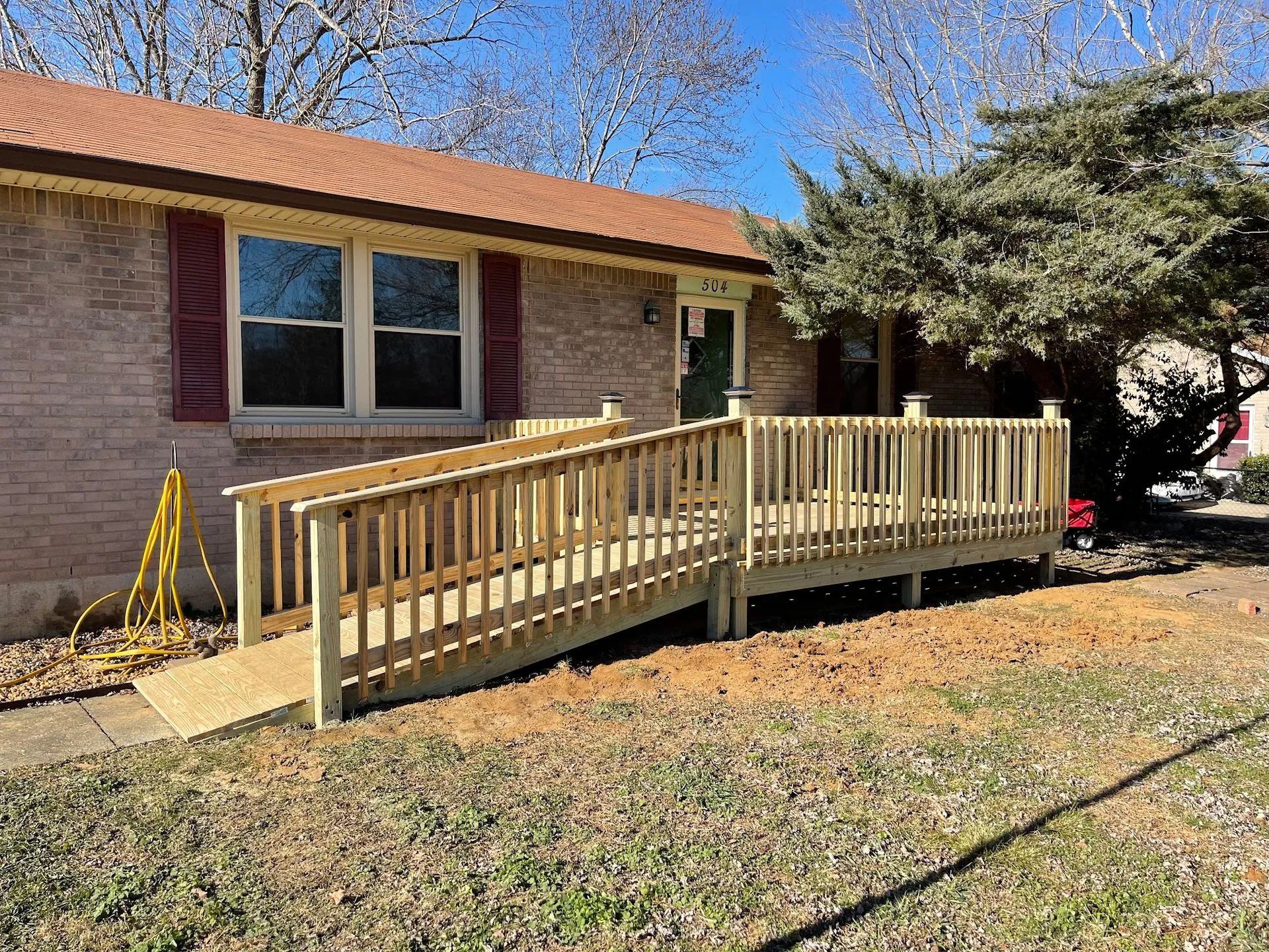 A wooden wheelchair ramp with railings leads up to the front door of a brick house.