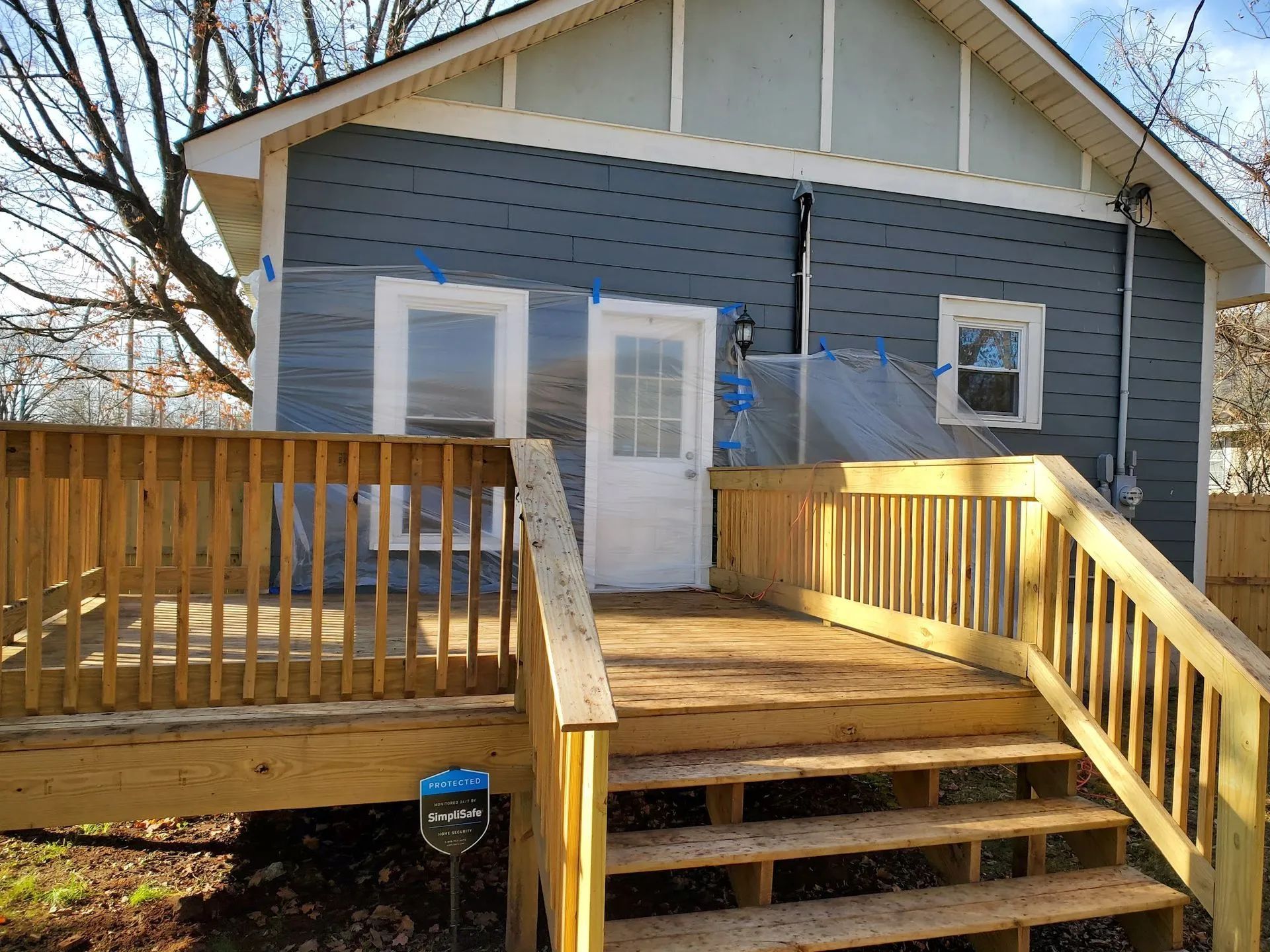 A newly built wooden deck with stairs attached to the side of a blue-sided house with a white door and windows.