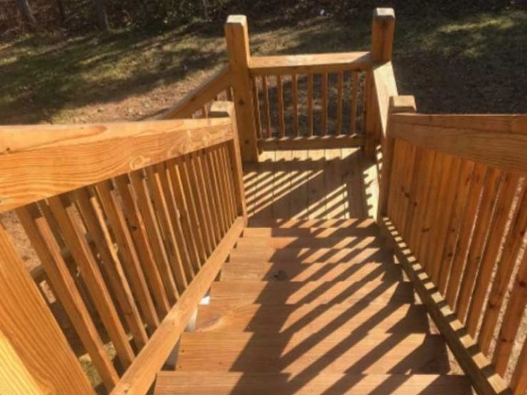 A view looking down a set of wooden stairs with railings leading to a landing outdoors.