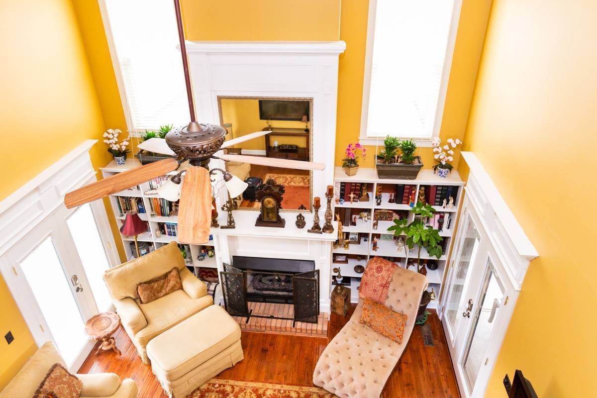 A high-angle view of a cozy yellow-walled living room with a fireplace, bookshelf, ceiling fan, and comfortable seating.
