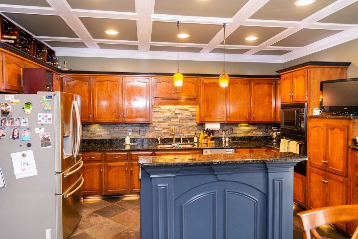 A kitchen with wooden cabinets, a dark blue island, black granite countertops, and a white coffered ceiling.