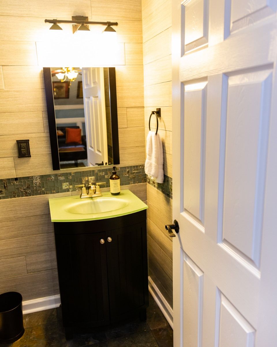 A small bathroom with a dark vanity, pale green countertop, mirror, overhead light, and a white towel hanging on the wall.