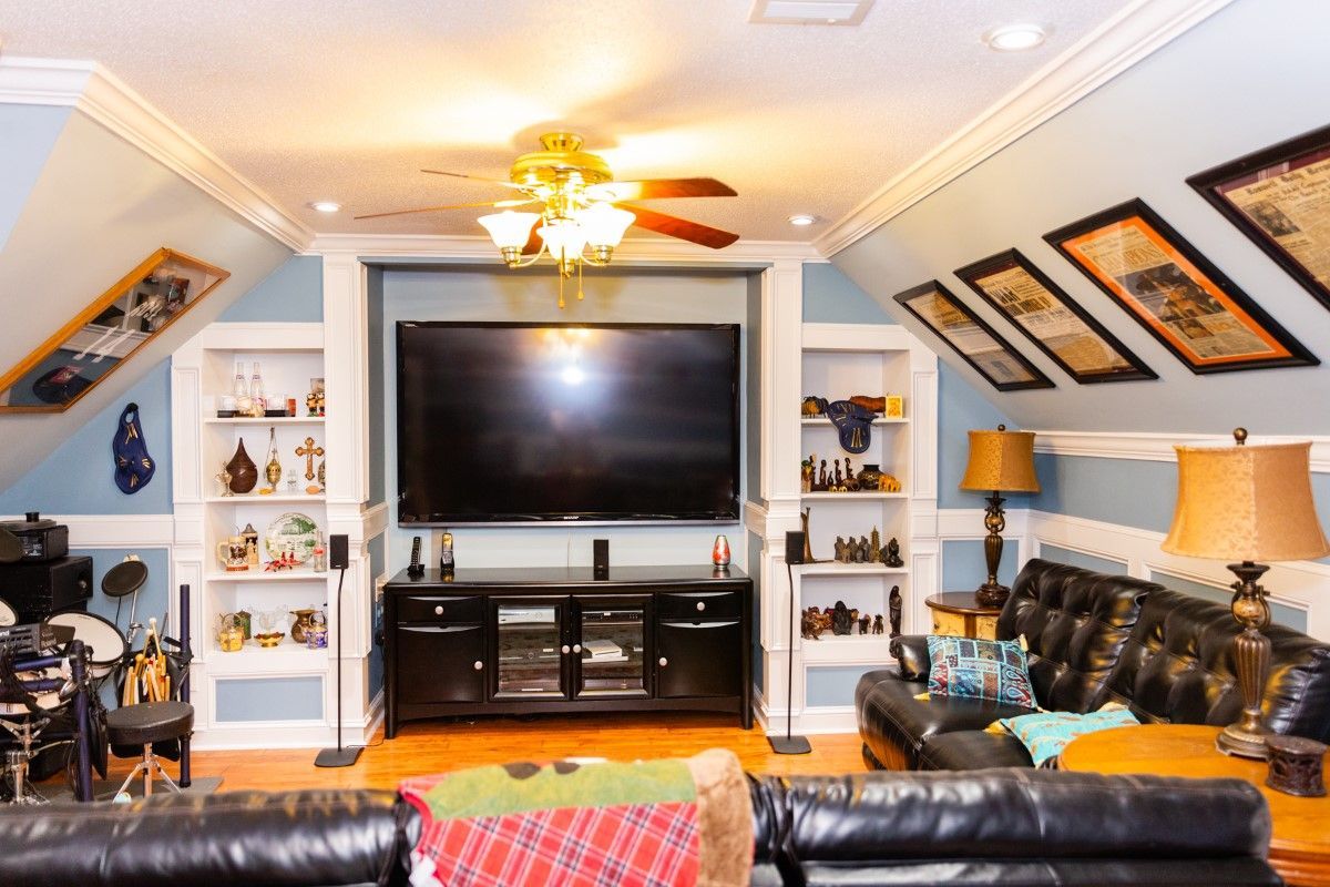A finished attic living area featuring a large TV centered between white shelving units and sloped walls with framed art.