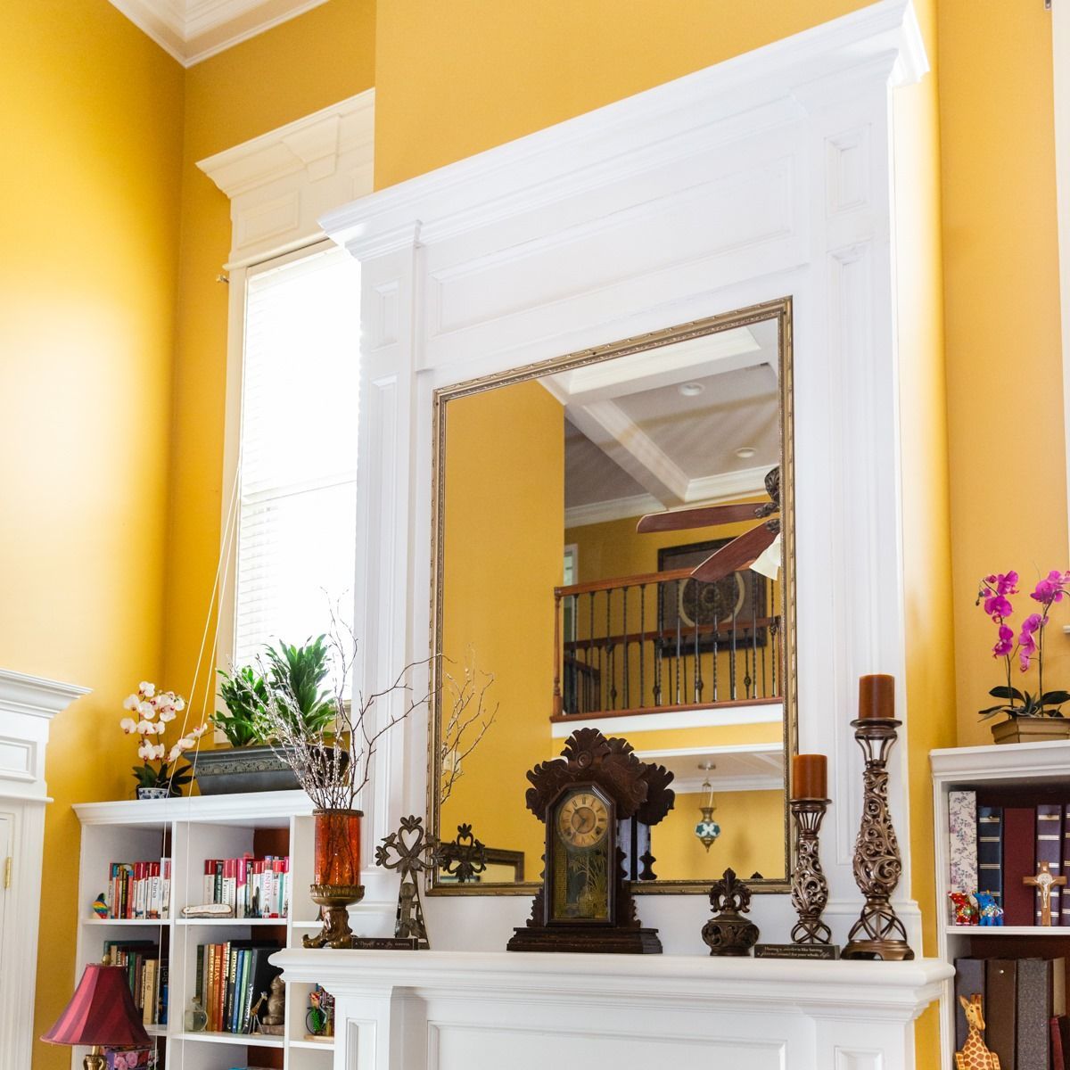 A tall white fireplace mantel with a large central mirror, decorated with a clock, candles, and yellow walls behind it.