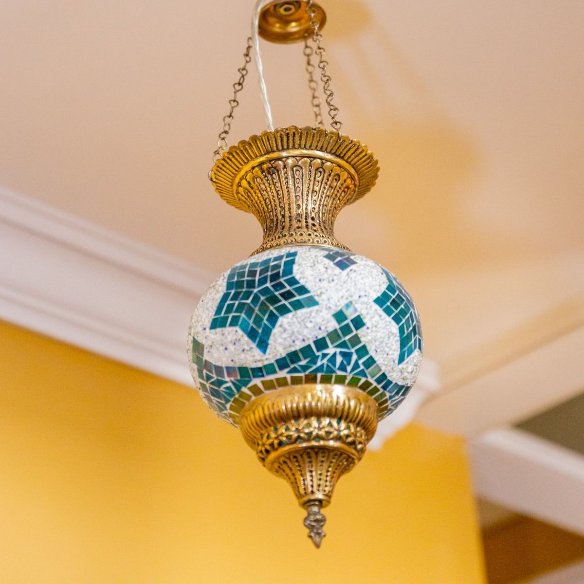 A hanging mosaic lamp with a brass top and bottom, featuring green star-shaped patterns against white glass tiles.