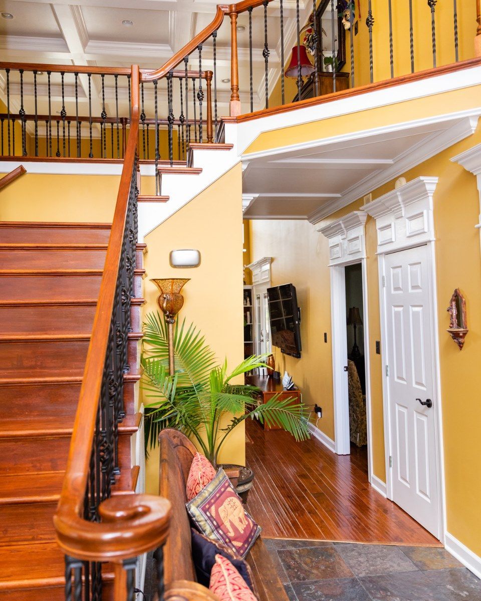 A staircase with wooden treads and ornate railings in a yellow foyer, leading to a hallway with white doors.