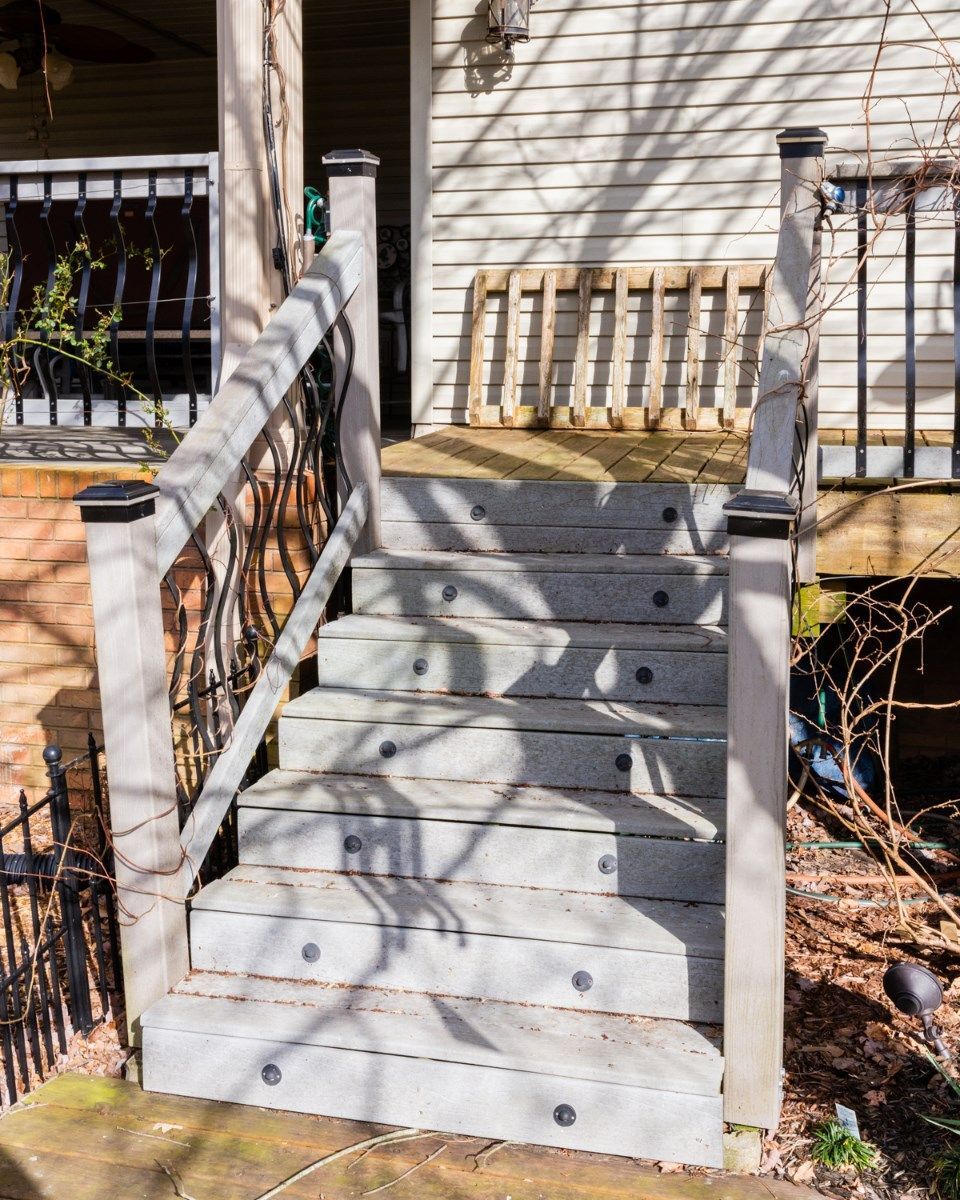 Outdoor staircase with gray steps, black metal railings, and integrated lights, leading to a wooden deck.