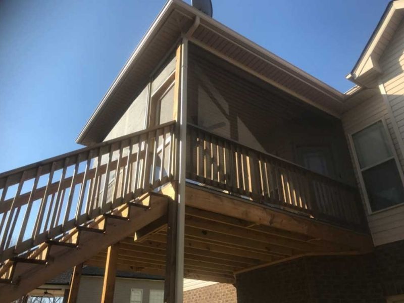 A wooden deck with a screened-in porch area and stairs leading down, attached to a two-story residential house.